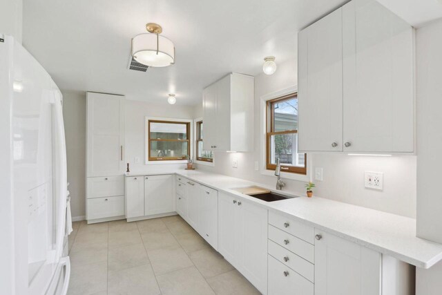 kitchen featuring freestanding refrigerator, light countertops, white cabinets, a sink, and light tile patterned floors