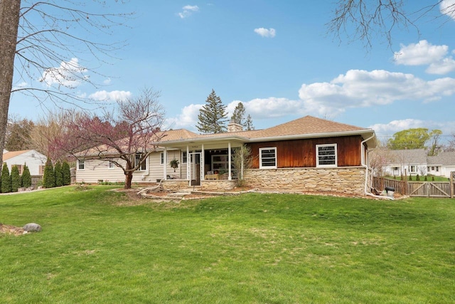 back of property featuring a yard, fence, a chimney, and stone siding