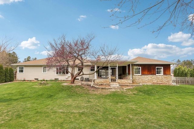 rear view of house featuring a lawn, fence, and stone siding