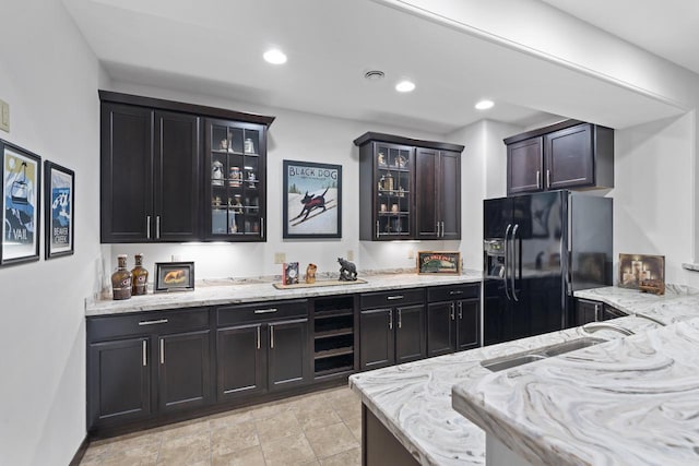 kitchen featuring a sink, black refrigerator with ice dispenser, light stone countertops, and glass insert cabinets