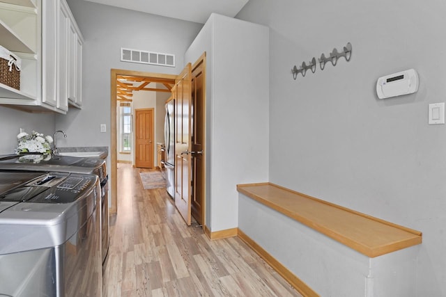 hall featuring visible vents, a sink, baseboards, light wood finished floors, and washer and dryer