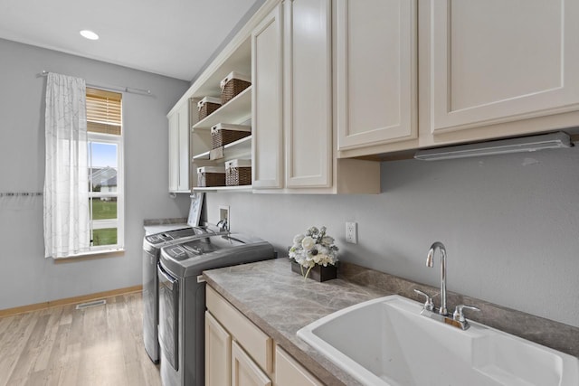 clothes washing area with cabinet space, a sink, baseboards, light wood-style floors, and separate washer and dryer