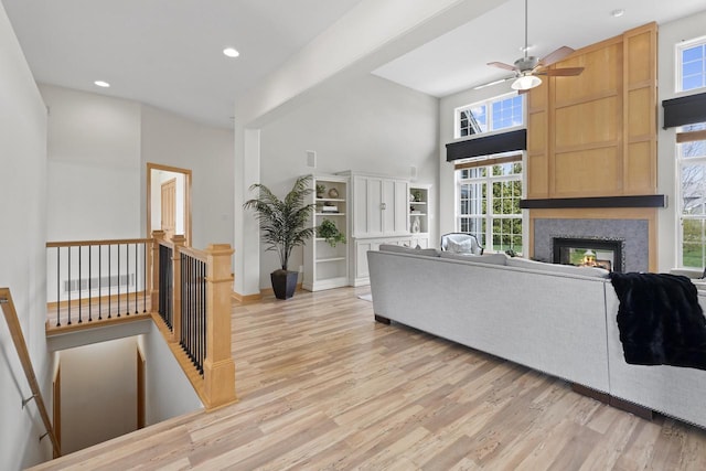 living room featuring a glass covered fireplace, a towering ceiling, recessed lighting, a ceiling fan, and light wood finished floors