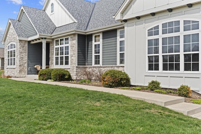 view of side of home with board and batten siding, a yard, a shingled roof, and stone siding