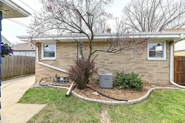 view of side of property featuring brick siding, fence, and cooling unit