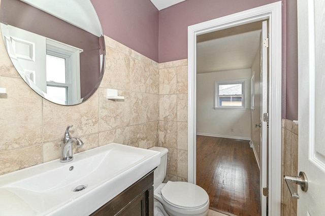 half bath with toilet, vanity, tile walls, and wood finished floors