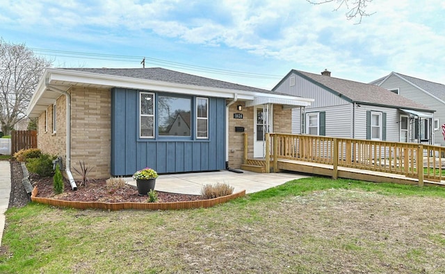 view of front of house with a deck, board and batten siding, a front yard, and roof with shingles