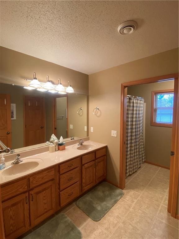 full bath with a textured ceiling, a sink, double vanity, visible vents, and tile patterned flooring