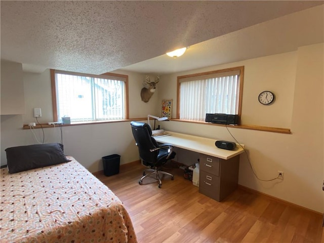 bedroom featuring light wood finished floors, a textured ceiling, and baseboards