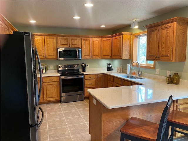 kitchen featuring brown cabinetry, stainless steel appliances, a peninsula, and a sink