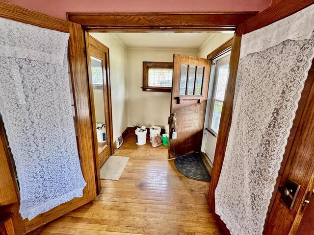 doorway with baseboards, ornamental molding, and light wood finished floors