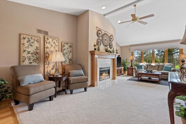 living area with beam ceiling, high vaulted ceiling, a glass covered fireplace, a ceiling fan, and visible vents