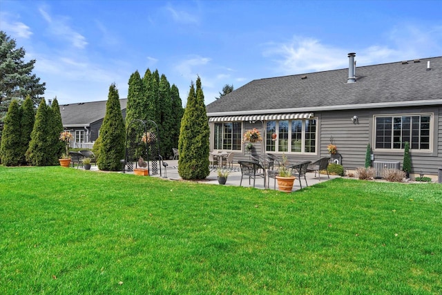 rear view of property featuring a patio, a lawn, and roof with shingles