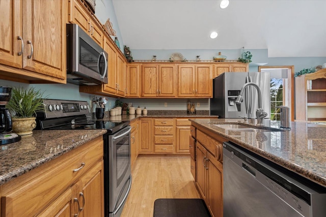 kitchen with recessed lighting, dark stone counters, stainless steel appliances, light wood finished floors, and a sink