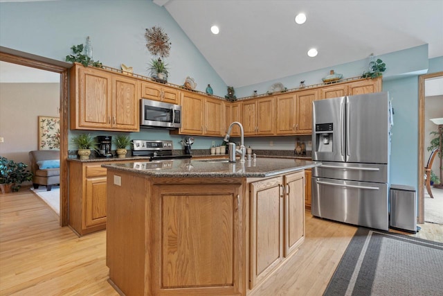 kitchen with dark stone counters, a sink, stainless steel appliances, high vaulted ceiling, and light wood-style flooring