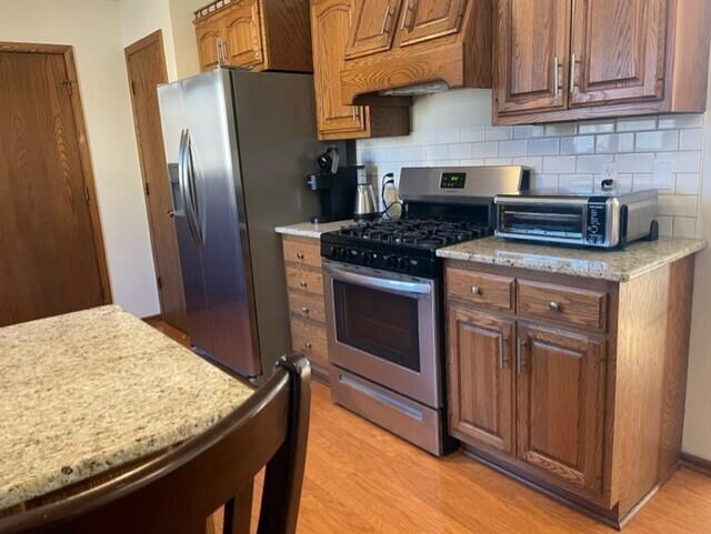 kitchen featuring a toaster, tasteful backsplash, stainless steel appliances, and light wood-style flooring