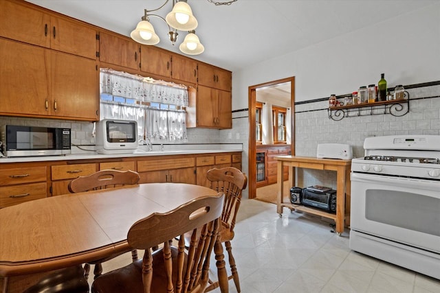 kitchen with brown cabinetry, white gas stove, light countertops, and stainless steel microwave