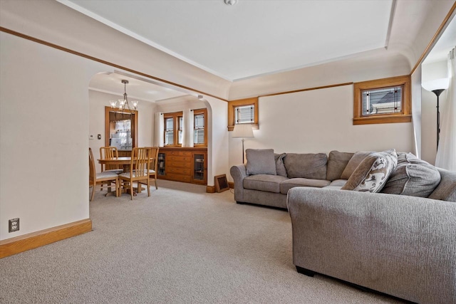 carpeted living area with a chandelier, baseboards, arched walkways, and ornamental molding