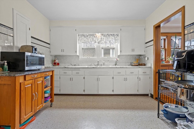 kitchen featuring stainless steel microwave, decorative backsplash, white cabinetry, and a sink