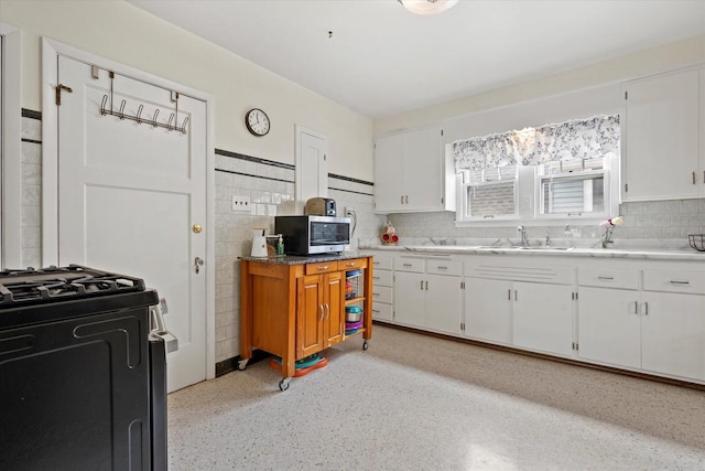 kitchen with white cabinetry, stainless steel microwave, gas range, and a sink