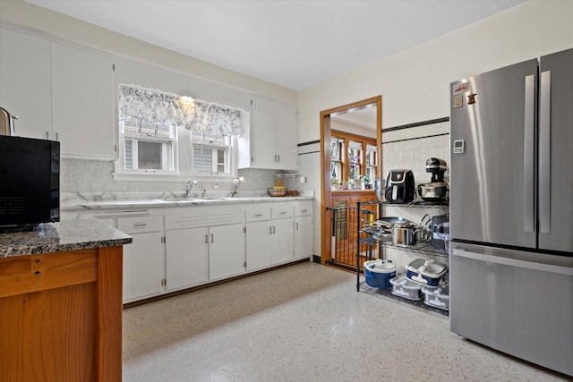 kitchen featuring tasteful backsplash, white cabinets, a sink, black microwave, and freestanding refrigerator