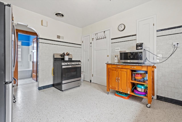 kitchen with tile walls, visible vents, arched walkways, and appliances with stainless steel finishes