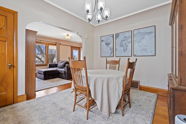 dining area with wood finished floors, an inviting chandelier, arched walkways, and crown molding