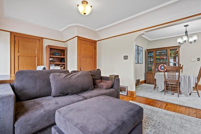 living room with ornamental molding, arched walkways, an inviting chandelier, and wood finished floors