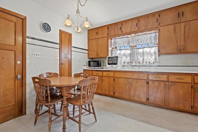 kitchen with stainless steel microwave, brown cabinets, decorative light fixtures, and light countertops