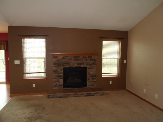 unfurnished living room featuring a stone fireplace, carpet, baseboards, and vaulted ceiling