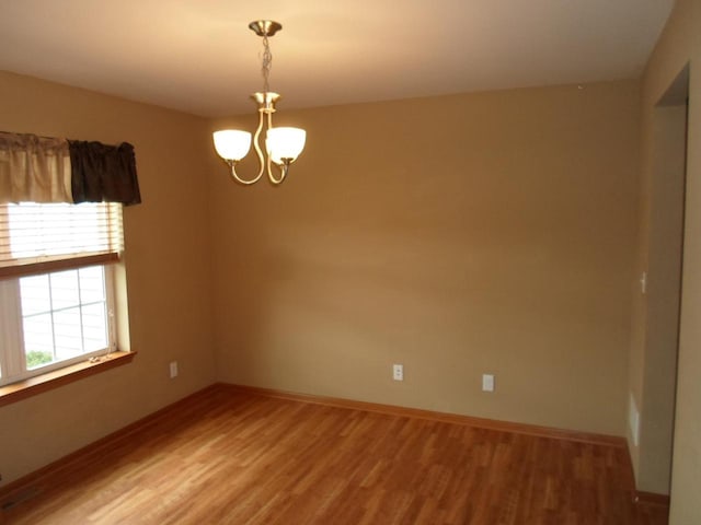 spare room featuring an inviting chandelier, baseboards, and light wood-style flooring