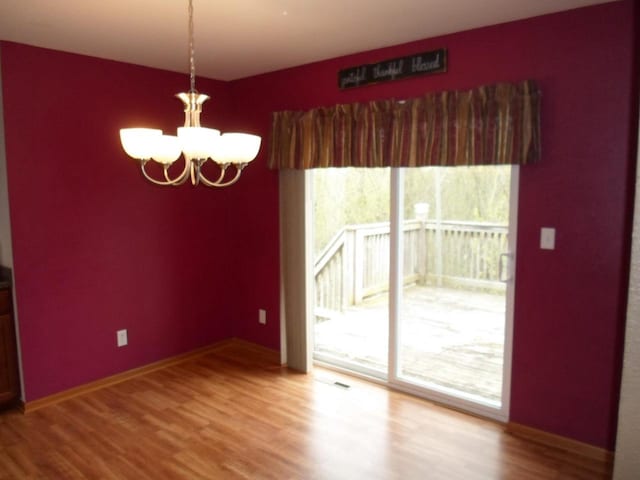 unfurnished dining area with baseboards, wood finished floors, and a chandelier