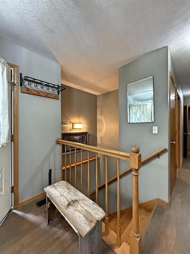 corridor with baseboards, a textured ceiling, wood finished floors, and an upstairs landing