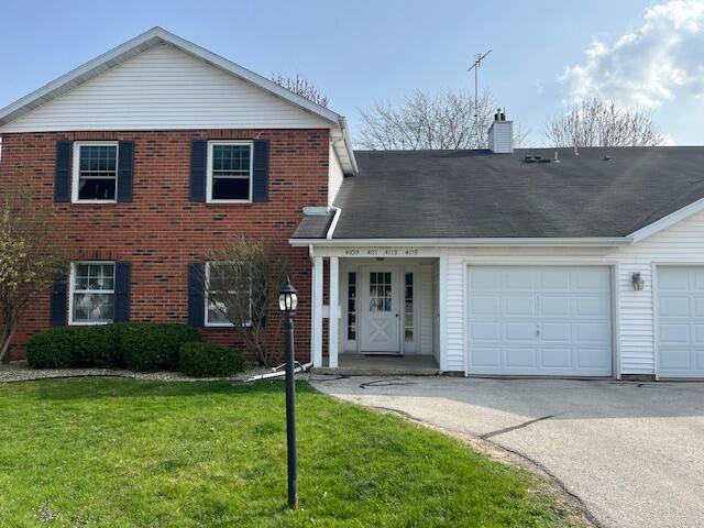 traditional-style house featuring a garage, a front lawn, a chimney, brick siding, and driveway