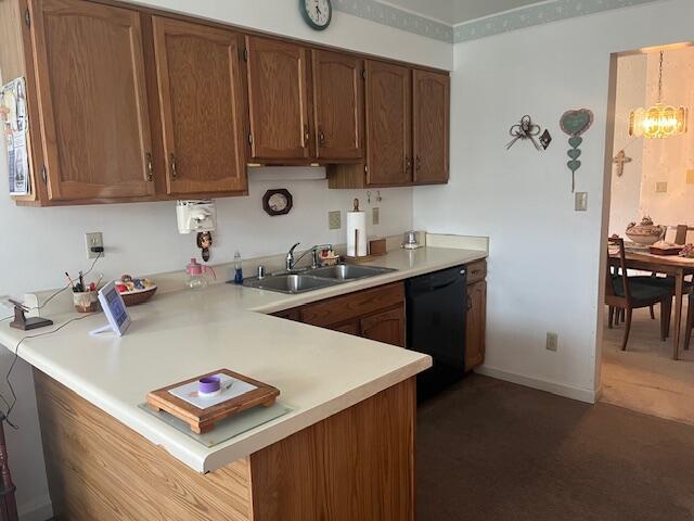 kitchen with a sink, dishwasher, light countertops, dark carpet, and a peninsula