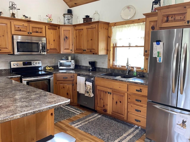 kitchen with brown cabinetry, backsplash, appliances with stainless steel finishes, a sink, and light wood-style flooring