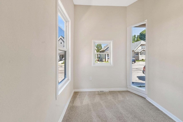 carpeted spare room with visible vents, baseboards, and a wealth of natural light