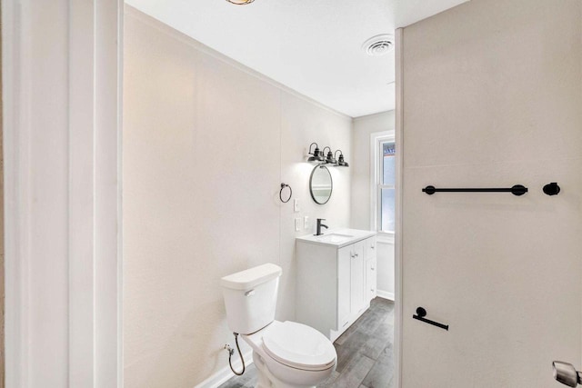 bathroom with vanity, toilet, baseboards, wood finished floors, and visible vents