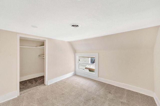unfurnished bedroom featuring visible vents, vaulted ceiling, baseboards, a closet, and light carpet