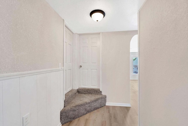 stairway featuring a textured wall, wainscoting, and wood finished floors