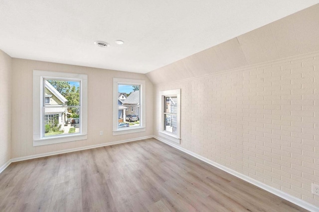 interior space featuring baseboards, vaulted ceiling, brick wall, and wood finished floors