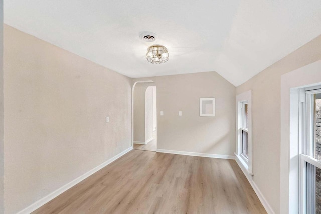 interior space with visible vents, baseboards, arched walkways, light wood-style flooring, and vaulted ceiling