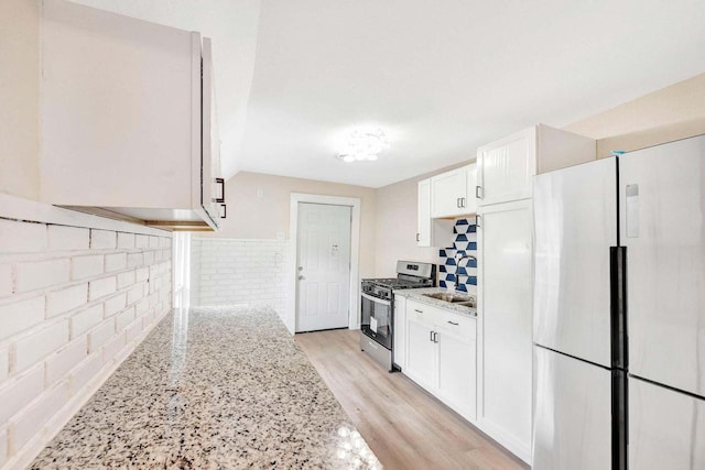 kitchen featuring freestanding refrigerator, decorative backsplash, light stone countertops, and stainless steel range with gas cooktop