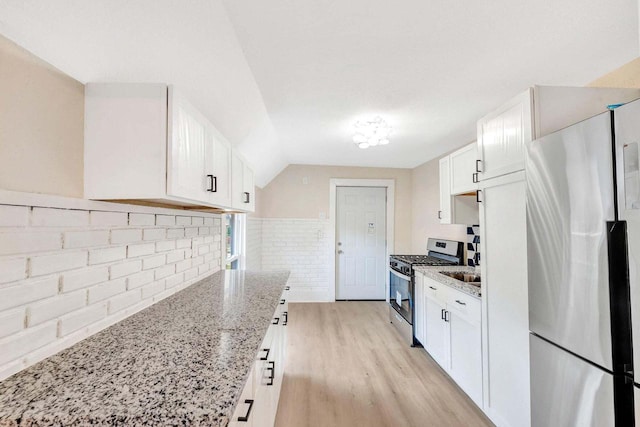 kitchen featuring appliances with stainless steel finishes, light stone countertops, light wood-type flooring, and white cabinetry