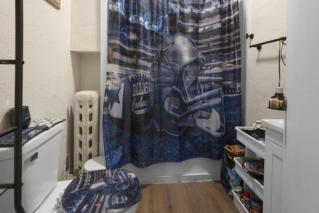 bathroom with toilet, a textured wall, and wood finished floors