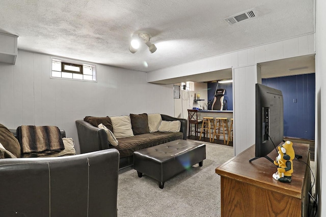living area featuring a textured ceiling, visible vents, light carpet, and a decorative wall