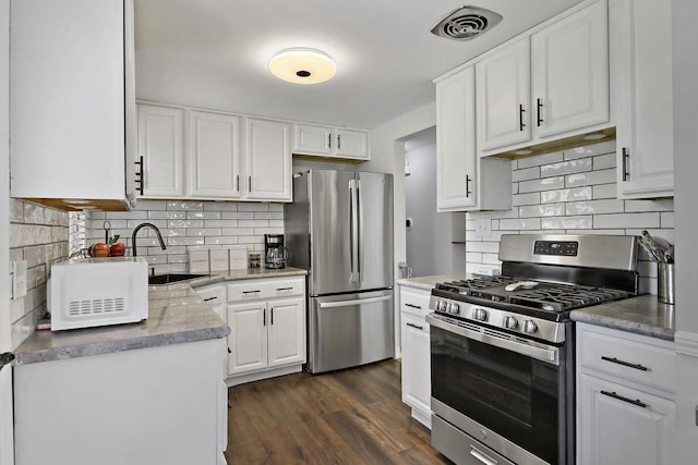 kitchen with appliances with stainless steel finishes, a sink, white cabinetry, decorative backsplash, and dark wood-style floors