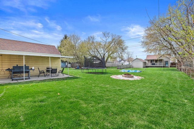 view of yard with a patio, a fenced backyard, a trampoline, and a fire pit