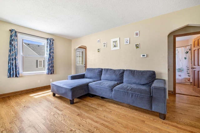living area featuring arched walkways, baseboards, light wood finished floors, and a textured ceiling