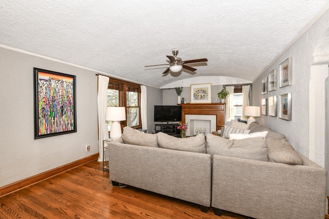 living area featuring a ceiling fan, a textured ceiling, vaulted ceiling, wood finished floors, and baseboards